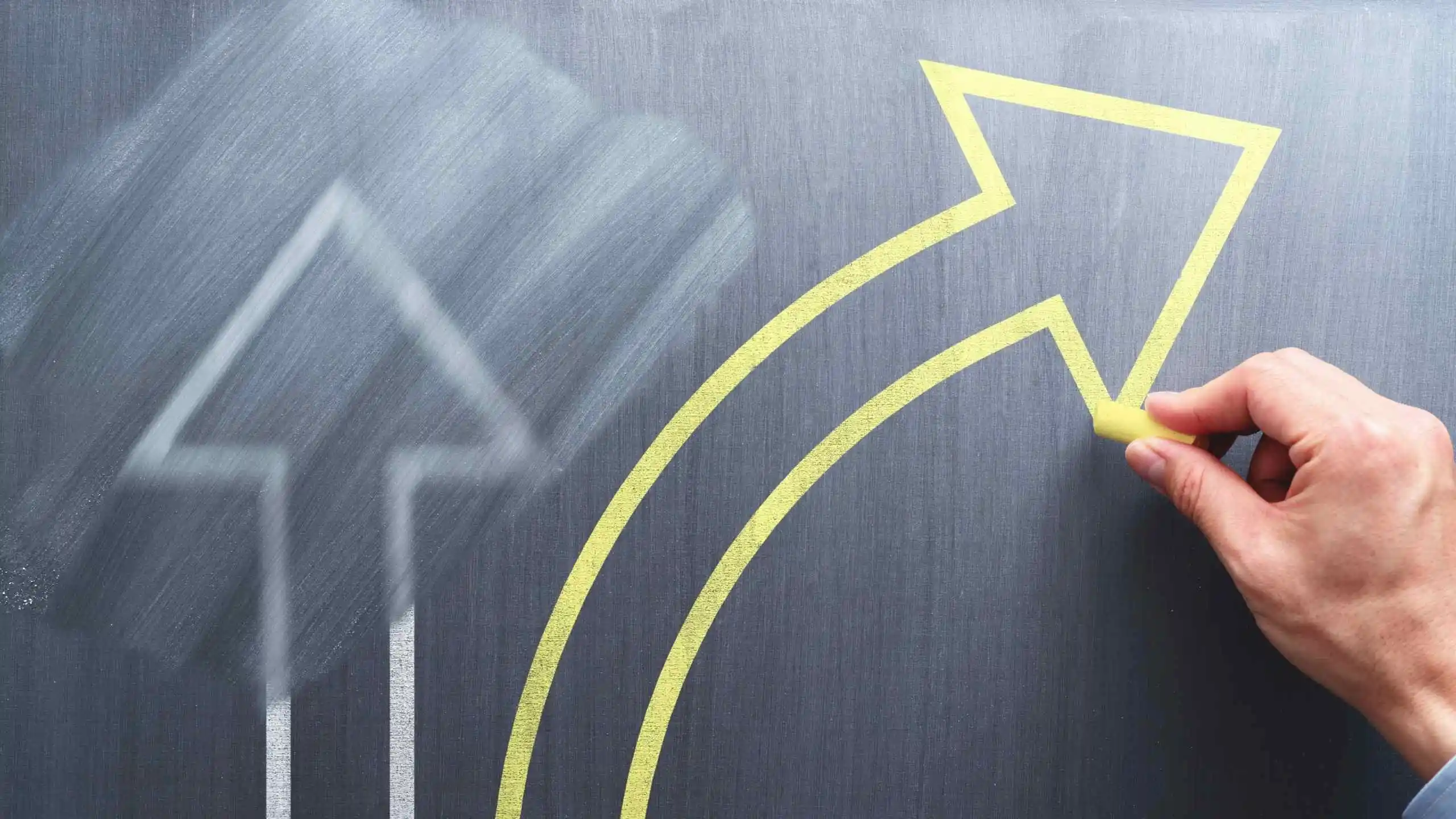 una flecha recta en uin tablero dibujada con tiza y borrada con descuido y otra flecha amarilla que se curva y está recién dibujada por una mano con tiza sanar heridas emocionales magui block