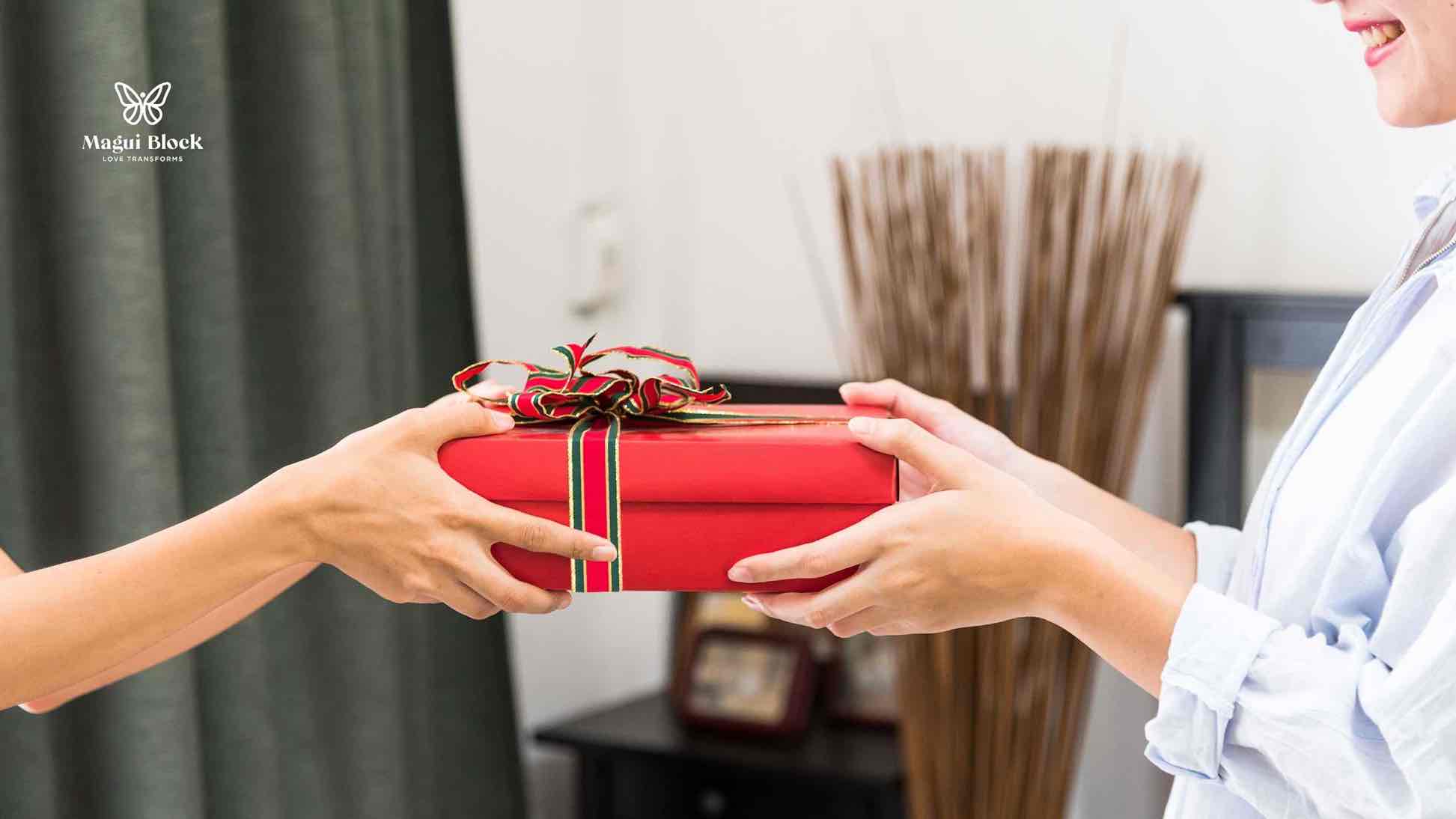 unas manos entregan regalo a una persona caja roja de regalo con moño sanar la familia magui block